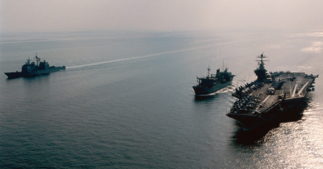 Aircraft carrier and two other navy vessels in the open sea.